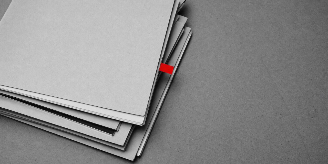 Ein Stapel gedruckter Dossiers, das oberste mit rotem Papierreiter markiert